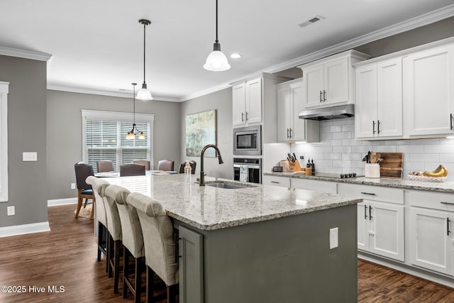 28 Winding Trl, Whispering Pines, NC 28327 - kitchen with appliances with stainless steel finishes, backsplash, dark wood-type flooring, a center island with sink, and ornamental molding
