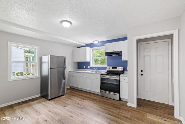 1415 Glenn St, Wilmington, NC 28401 - kitchen featuring stainless steel appliances, under cabinet range hood, white cabinetry, light wood-type flooring, and a textured ceiling