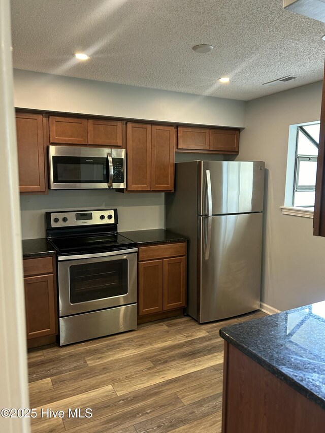 106 Quarterdeck Townes Townes Unit 106, New Bern, NC 28562 - kitchen with appliances with stainless steel finishes, dark countertops, a textured ceiling, dark wood-style flooring, and brown cabinetry