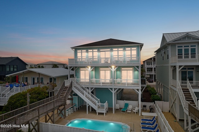 328 E First St, Ocean Isle Beach, NC 28469 - back of house at dusk with stairs, a patio, a fenced backyard, and a balcony
