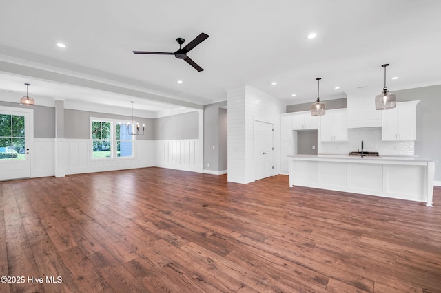 5988 Gray Squirrel Path, Southport, NC 28461 - unfurnished living room featuring dark wood-style floors, ceiling fan, wainscoting, a chandelier, and recessed lighting