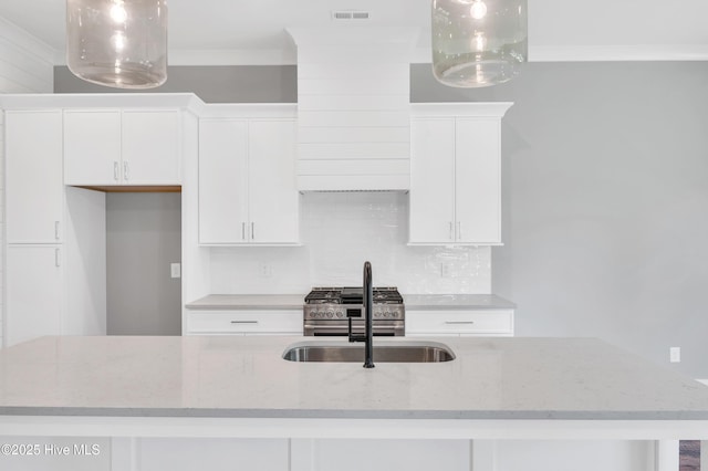 5988 Gray Squirrel Path, Southport, NC 28461 - kitchen with white cabinets, tasteful backsplash, crown molding, stainless steel stove, and an island with sink