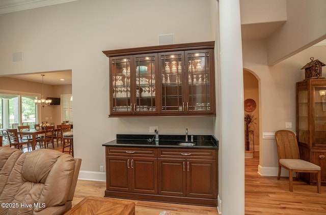 545 Gladstone Cir SW, Ocean Isle Beach, NC 28469 - indoor wet bar featuring light wood-style floors, arched walkways, a chandelier, pendant lighting, and a high ceiling