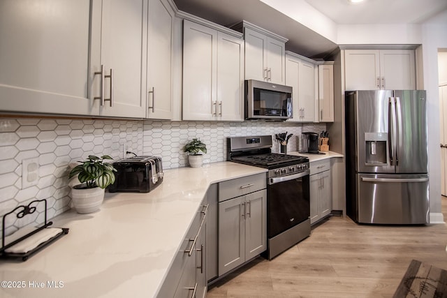 440 Bramble Ln, Clayton, NC 27527 - kitchen featuring appliances with stainless steel finishes, gray cabinetry, light wood-type flooring, tasteful backsplash, and light stone countertops