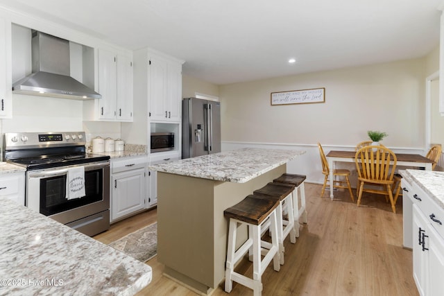 84 White Pine Rd, Lake Waccamaw, NC 28450 - kitchen with wall chimney range hood, appliances with stainless steel finishes, light wood-style floors, white cabinetry, and a kitchen breakfast bar