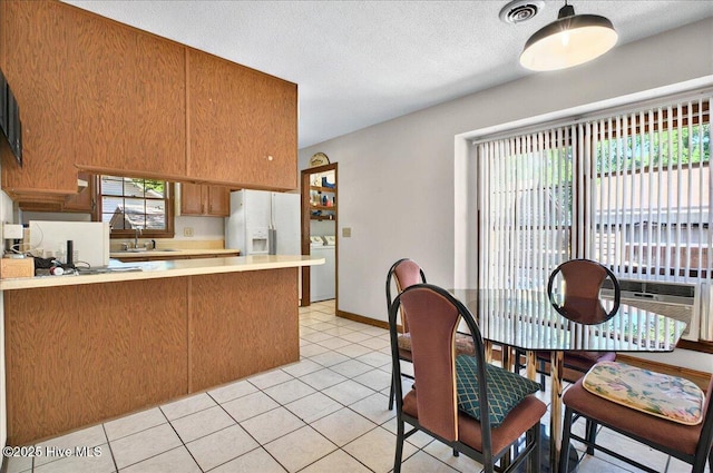 163 NW 9th St, Oak Island, NC 28465 - kitchen with a peninsula, light countertops, brown cabinets, light tile patterned floors, and white fridge with ice dispenser