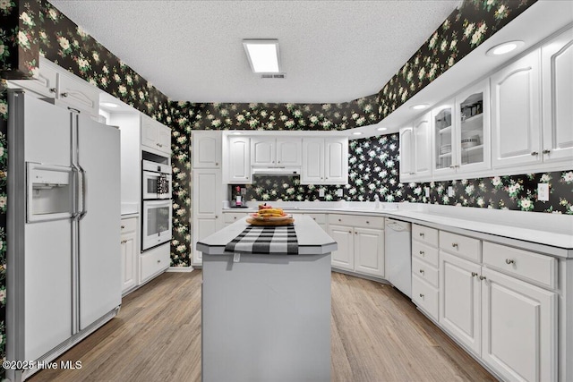 1610 Winding Way SW, Ocean Isle Beach, NC 28469 - kitchen featuring white appliances, wallpapered walls, white cabinets, light wood-type flooring, and glass insert cabinets