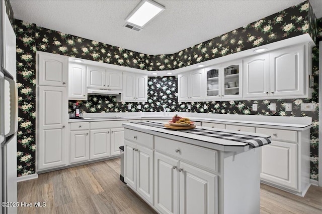 1610 Winding Way SW, Ocean Isle Beach, NC 28469 - kitchen featuring wallpapered walls, light wood-type flooring, a textured ceiling, white cabinetry, and light countertops