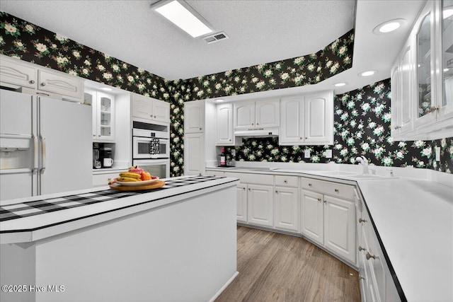 1610 Winding Way SW, Ocean Isle Beach, NC 28469 - kitchen featuring wallpapered walls, white appliances, under cabinet range hood, white cabinets, and light wood-style floors