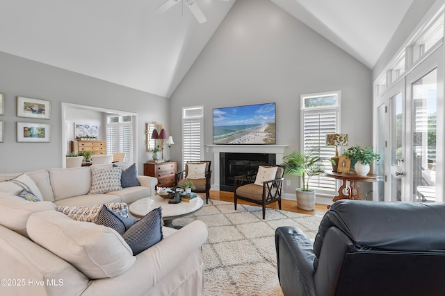 188 Edgewater Cir, Sunset Beach, NC 28468 - living room featuring high vaulted ceiling, light wood finished floors, a ceiling fan, and a glass covered fireplace