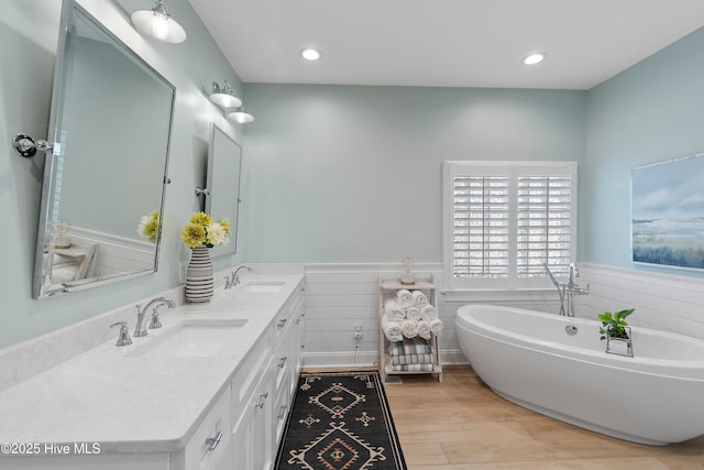 188 Edgewater Cir, Sunset Beach, NC 28468 - bathroom with a wainscoted wall, double vanity, a freestanding bath, wood finished floors, and recessed lighting