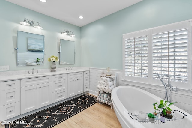 188 Edgewater Cir, Sunset Beach, NC 28468 - bathroom with double vanity, a freestanding bath, recessed lighting, wood finished floors, and a wainscoted wall