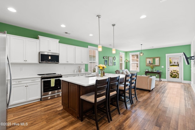 9154 Village Lake Dr SW, Calabash, NC 28467 - kitchen with stainless steel appliances, a kitchen breakfast bar, light countertops, dark wood-style flooring, and white cabinets