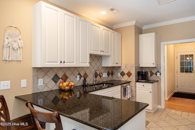 4725 Wedgefield Dr, Wilmington, NC 28409 - kitchen with a breakfast bar area, dark stone counters, a peninsula, white cabinetry, and crown molding