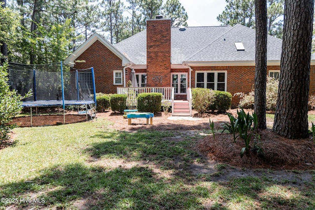 4725 Wedgefield Dr, Wilmington, NC 28409 - rear view of property with a trampoline, a wooden deck, roof with shingles, brick siding, and a yard
