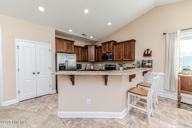 276 Widgeon Way, Lillington, NC 27546 - kitchen featuring appliances with stainless steel finishes, vaulted ceiling, light stone counters, a breakfast bar area, and a peninsula