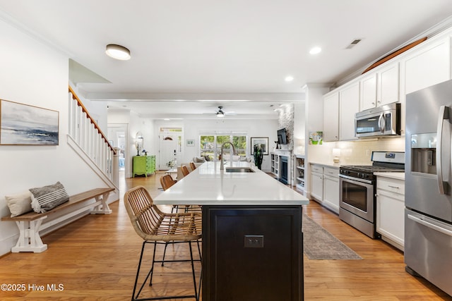 8203 Brays Dr, Wilmington, NC 28411 - kitchen featuring appliances with stainless steel finishes, a breakfast bar, a ceiling fan, a kitchen island with sink, and light wood finished floors