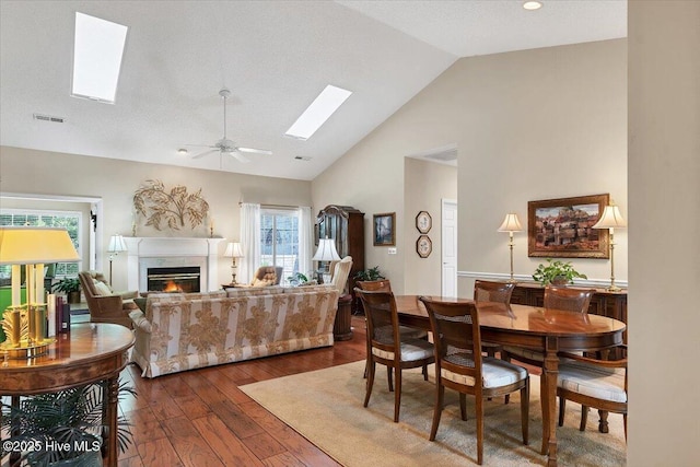 1 Pine Crest Dr, Whispering Pines, NC 28327 - living room featuring a skylight, dark wood-style floors, high vaulted ceiling, a warm lit fireplace, and a ceiling fan