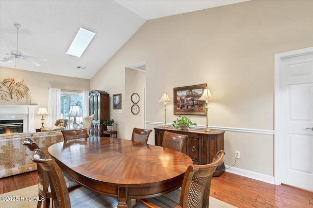 1 Pine Crest Dr, Whispering Pines, NC 28327 - dining room featuring hardwood / wood-style flooring, a ceiling fan, a warm lit fireplace, high vaulted ceiling, and a skylight