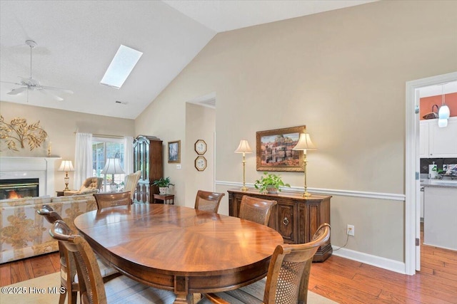 1 Pine Crest Dr, Whispering Pines, NC 28327 - dining room featuring light wood-style flooring, a ceiling fan, a glass covered fireplace, a skylight, and high vaulted ceiling