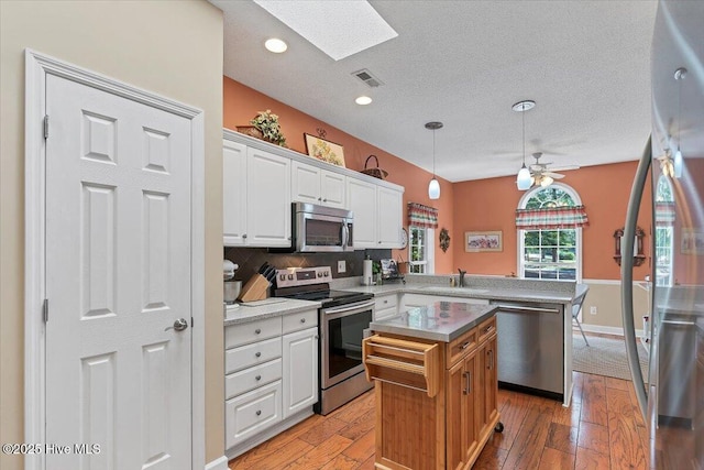 1 Pine Crest Dr, Whispering Pines, NC 28327 - kitchen with appliances with stainless steel finishes, a peninsula, white cabinets, a skylight, and a textured ceiling