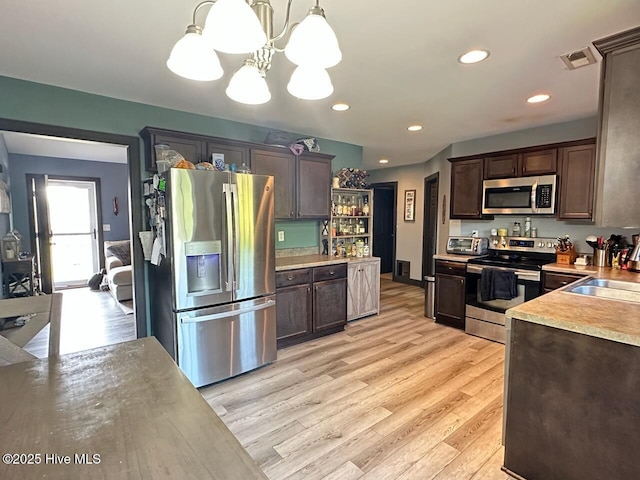 202 Oak Ridge Ln, Holly Ridge, NC 28445 - kitchen with appliances with stainless steel finishes, dark brown cabinetry, light wood-type flooring, light countertops, and a chandelier