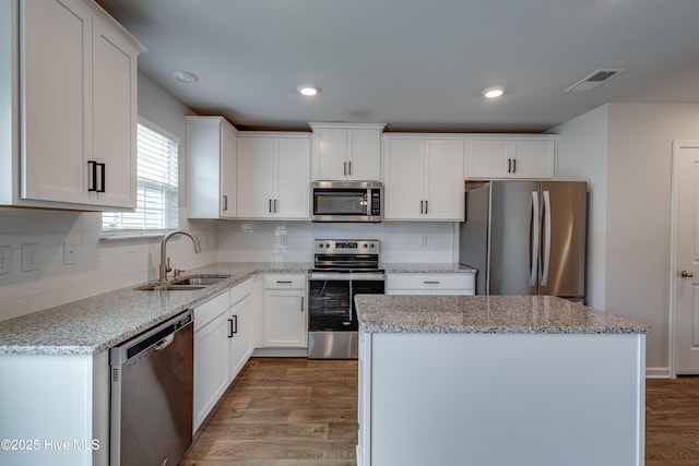 411 Isabelle St, New Bern, NC 28560 - kitchen with appliances with stainless steel finishes, wood finished floors, white cabinets, a kitchen island, and light stone countertops