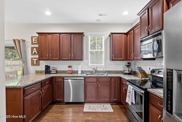3243 Kellerton Pl, Wilmington, NC 28409 - kitchen featuring appliances with stainless steel finishes, a peninsula, light stone countertops, dark wood-style floors, and backsplash