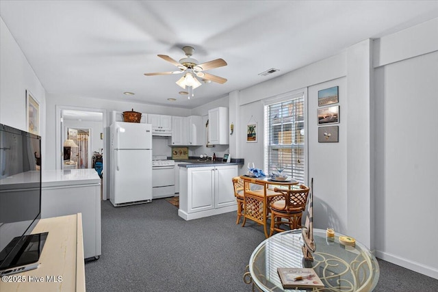 104 NE 27th St, Oak Island, NC 28465 - kitchen with white appliances, dark colored carpet, white cabinets, ceiling fan, and under cabinet range hood