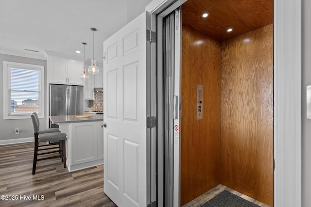130 Raleigh St, Holden Beach, NC 28462 - kitchen featuring elevator, stainless steel fridge, wood finished floors, white cabinetry, and a kitchen bar