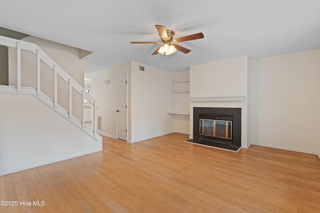 514 Cobblestone Dr, Wilmington, NC 28405 - unfurnished living room featuring ceiling fan, light wood-type flooring, a glass covered fireplace, and stairs