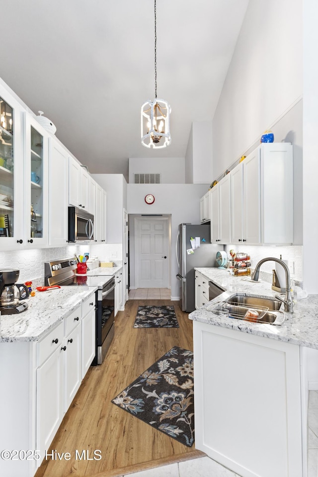102 Crooked Gulley Cir, Sunset Beach, NC 28468 - kitchen with stainless steel appliances, a chandelier, white cabinets, light wood-type flooring, and decorative backsplash