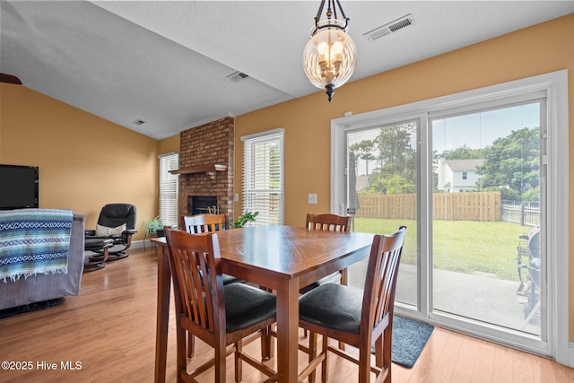 1005 Pleasant Dale Dr, Wilmington, NC 28412 - dining room with vaulted ceiling, light wood-style floors, a fireplace, a textured ceiling, and a chandelier