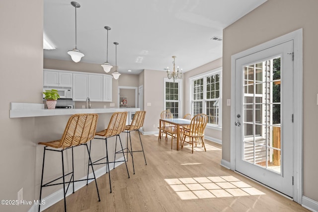 324 Foster Creek Rd, Swansboro, NC 28584 - kitchen with white microwave, white cabinetry, a kitchen breakfast bar, a chandelier, and light wood-style flooring
