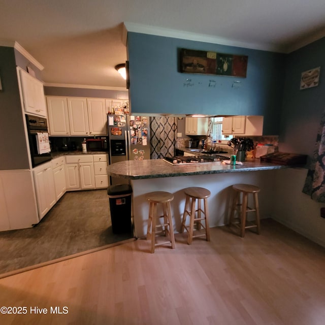 204 Tyree Rd, Kinston, NC 28504 - kitchen featuring black appliances, a peninsula, dark countertops, dark wood finished floors, and white cabinets