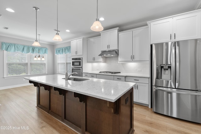 2955 Moorings Way SE, Southport, NC 28461 - kitchen featuring appliances with stainless steel finishes, under cabinet range hood, backsplash, light wood-type flooring, and an island with sink