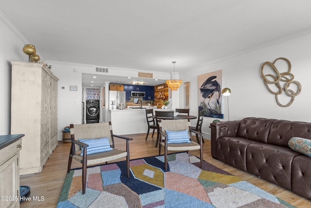 8801 Reed Dr Unit 303W, Emerald Isle, NC 28594 - living room featuring washer / clothes dryer, ornamental molding, light wood-type flooring, and a chandelier