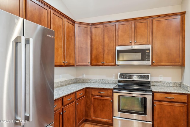 3716 Pond Pine Ct, Southport, NC 28461 - kitchen with stainless steel appliances, lofted ceiling, light stone countertops, brown cabinetry, and light wood-style floors