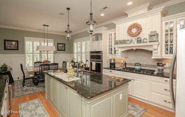 595 Wicklow Sq SW, Ocean Isle Beach, NC 28469 - kitchen featuring stainless steel appliances, light wood finished floors, an island with sink, a wainscoted wall, and pendant lighting