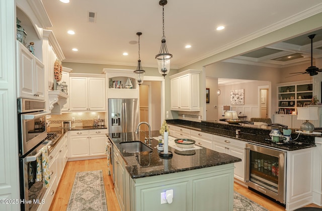 595 Wicklow Sq SW, Ocean Isle Beach, NC 28469 - kitchen with beverage cooler, appliances with stainless steel finishes, a kitchen island with sink, ceiling fan, and light wood-type flooring