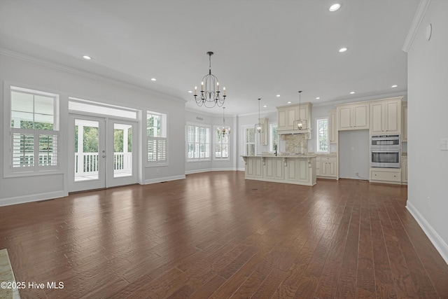 311 S Kingfisher Ln, Hampstead, NC 28443 - unfurnished living room featuring a chandelier, plenty of natural light, dark wood-style flooring, ornamental molding, and french doors