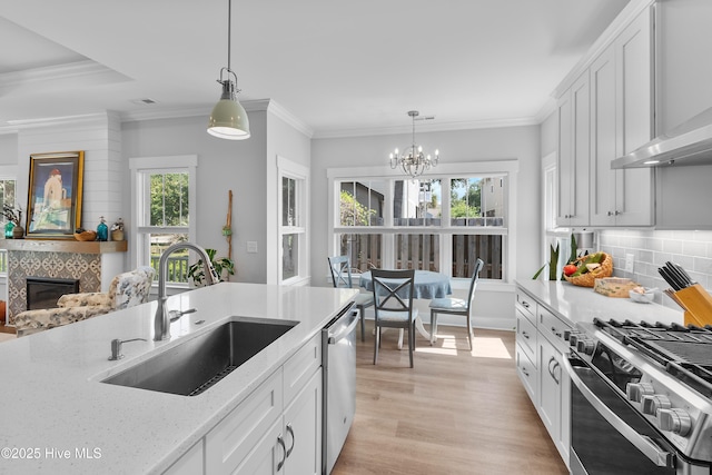 102 SW 4th St, Oak Island, NC 28465 - kitchen with wall chimney range hood, appliances with stainless steel finishes, a tile fireplace, a chandelier, and light wood-type flooring