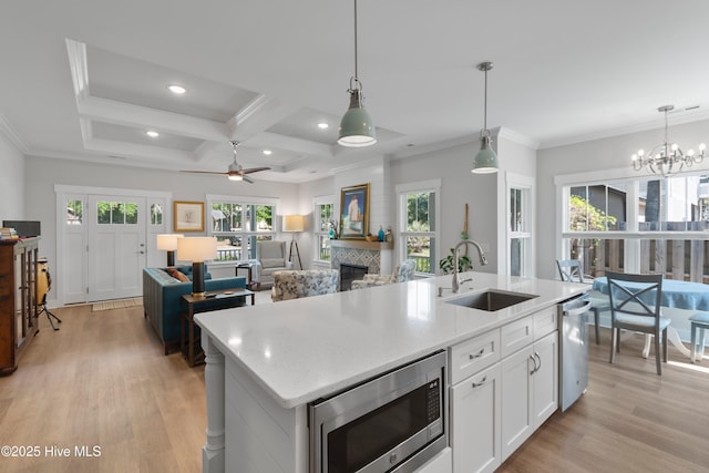 102 SW 4th St, Oak Island, NC 28465 - kitchen featuring appliances with stainless steel finishes, light wood-style flooring, a fireplace, coffered ceiling, and white cabinetry