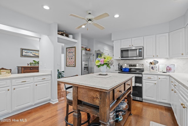 111 Mcginnis Dr, Pine Knoll Shores, NC 28512 - kitchen with stainless steel appliances, light wood-style floors, ceiling fan, decorative backsplash, and white cabinets
