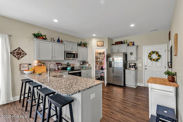 103 Baymeade Ct, Peletier, NC 28584 - kitchen featuring stainless steel appliances, dark wood-style flooring, a peninsula, light stone countertops, and a kitchen bar