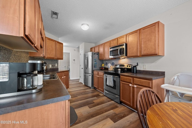 2950 Judge Manly Dr, New Bern, NC 28562 - kitchen featuring appliances with stainless steel finishes, dark countertops, dark wood-type flooring, decorative backsplash, and a textured ceiling