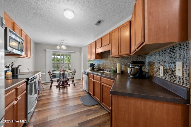 2950 Judge Manly Dr, New Bern, NC 28562 - kitchen with stainless steel appliances, dark countertops, light wood-style flooring, backsplash, and brown cabinetry