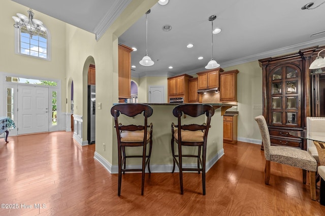 90 Shadow Creek Ct, Pinehurst, NC 28374 - kitchen featuring brown cabinets, a kitchen bar, ornamental molding, arched walkways, and wood-type flooring