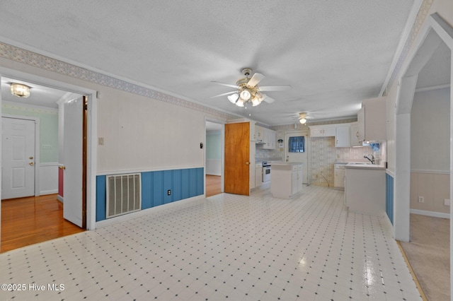 1603 Laurel St, Goldsboro, NC 27530 - unfurnished living room featuring ceiling fan, ornamental molding, a wainscoted wall, a textured ceiling, and light floors