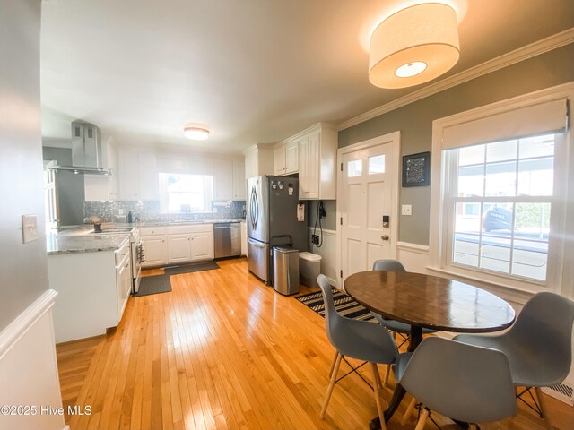 1721 Nash St NW, Wilson, NC 27893 - kitchen with wall chimney exhaust hood, appliances with stainless steel finishes, white cabinetry, tasteful backsplash, and light wood finished floors